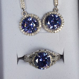 May include: A set of silver earrings and a ring featuring a large, round, purple gemstone encircled by smaller, clear gemstones.