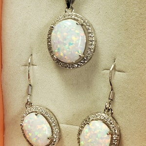 May include: A silver necklace and earrings set with a white opal stone surrounded by a halo of smaller stones.