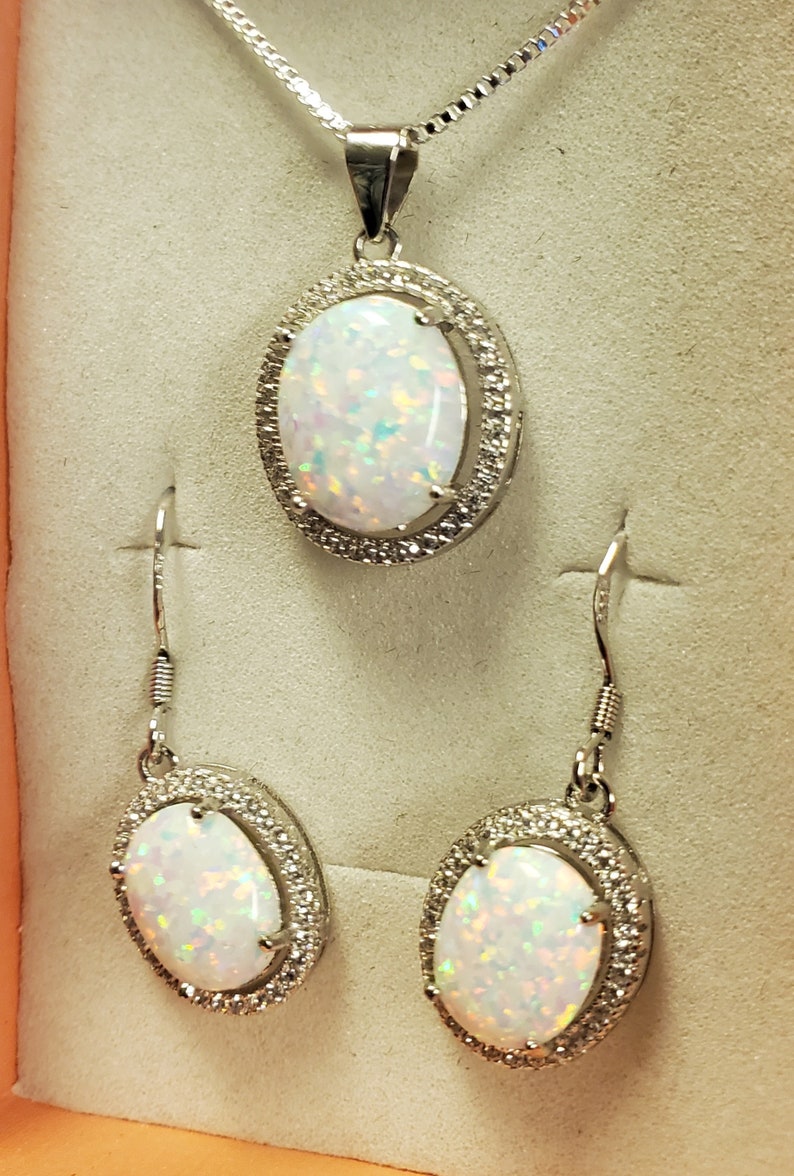 May include: A silver necklace and earrings set with a white opal stone surrounded by a halo of smaller stones.