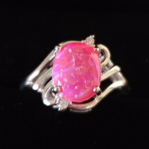 May include: A silver ring with a pink opal gemstone set in a swirling design. The ring has small clear accent stones.
