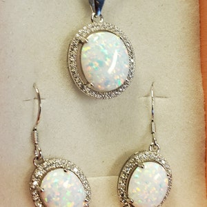 May include: A silver necklace with a white opal pendant surrounded by small clear stones. Matching earrings with white opals and clear stones.