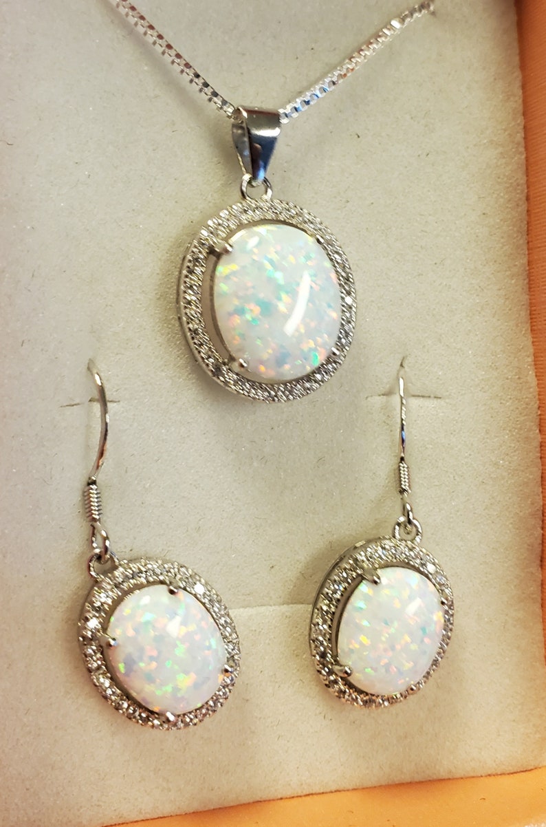 May include: A silver necklace with a white opal pendant surrounded by small clear stones. Matching earrings with white opals and clear stones.