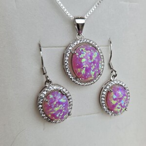 May include: A silver necklace and earrings set with a pink opal stone surrounded by a halo of clear cubic zirconia stones.