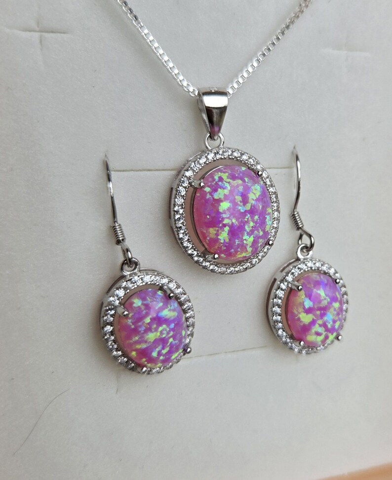 May include: A silver necklace and earrings set with a pink opal stone surrounded by a halo of clear cubic zirconia stones.