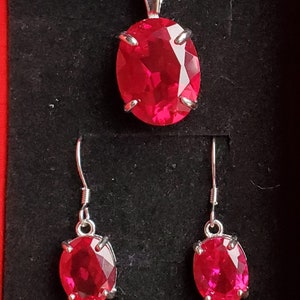 Puede incluir: Un conjunto de joyas de rub&iacute; que incluye un collar con colgante y pendientes a juego. Las piedras de rub&iacute; de forma ovalada est&aacute;n engastadas en plata y tienen un color rojo brillante.