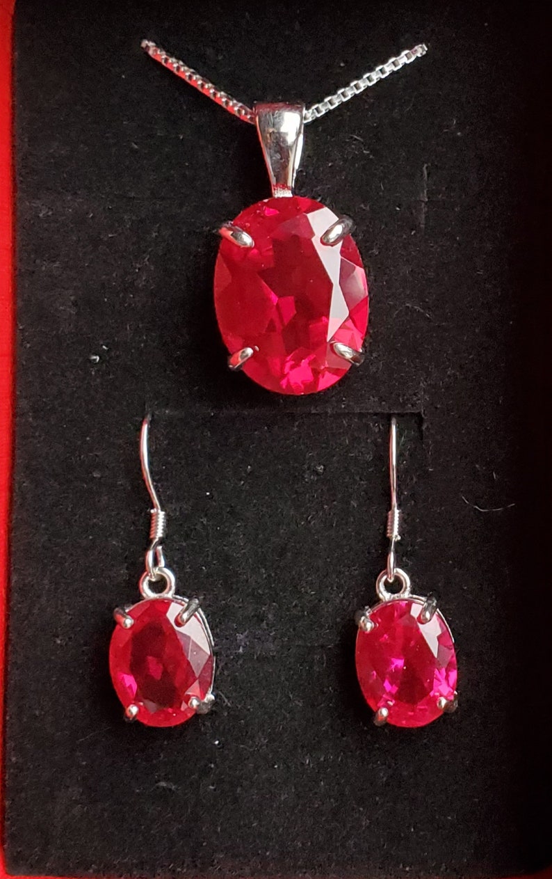 Puede incluir: Un conjunto de joyas de rub&iacute; que incluye un collar con colgante y pendientes a juego. Las piedras de rub&iacute; de forma ovalada est&aacute;n engastadas en plata y tienen un color rojo brillante.