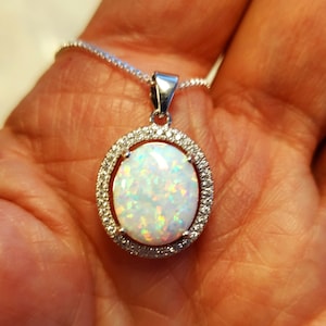 May include: A silver chain necklace with a white opal pendant set in a silver oval frame with small clear stones around the edge.