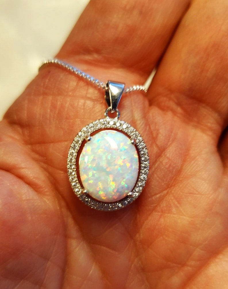 May include: A silver chain necklace with a white opal pendant set in a silver oval frame with small clear stones around the edge.