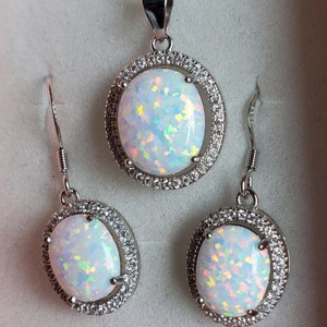 May include: A white opal necklace and earrings set with a silver chain and oval-shaped stones surrounded by a halo of smaller stones.