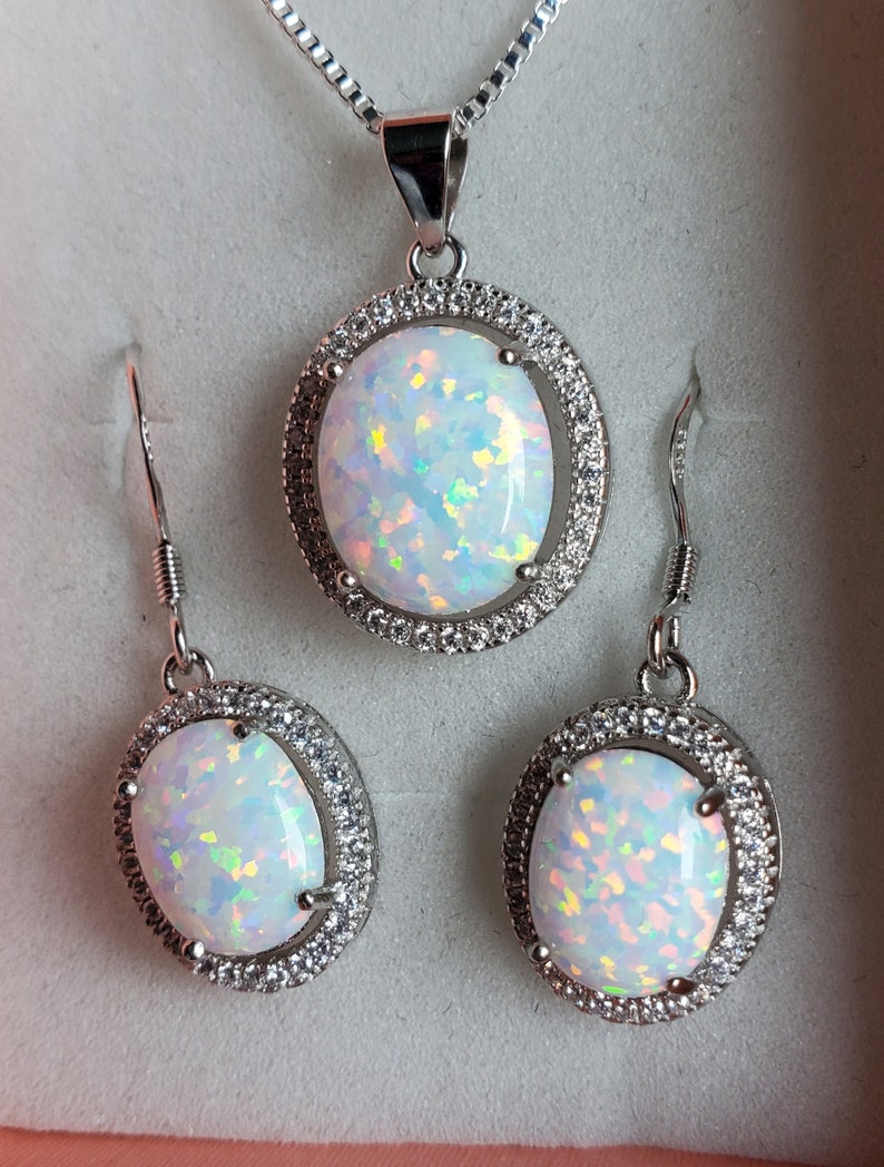 May include: A white opal necklace and earrings set with a silver chain and oval-shaped stones surrounded by a halo of smaller stones.