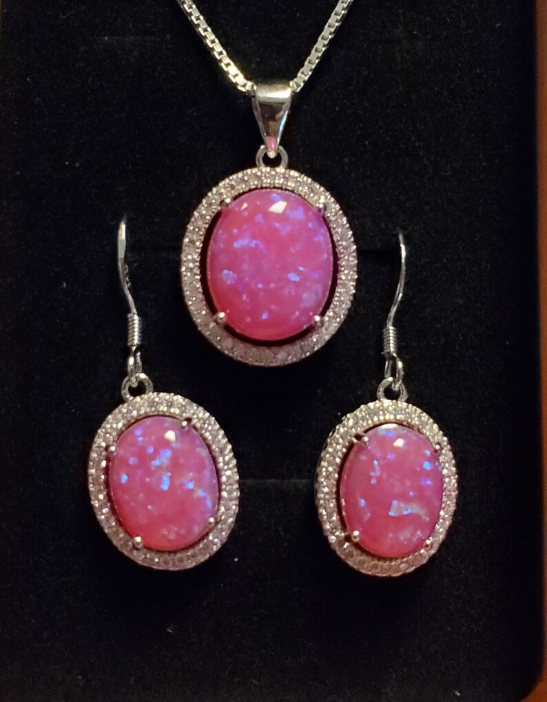 Puede incluir: Un collar con colgante de &oacute;palo rosa y un juego de pendientes a juego. El colgante y los pendientes tienen un engaste ovalado de plata con un halo de peque&ntilde;as piedras transparentes alrededor del &oacute;palo rosa.