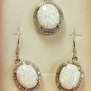 May include: A silver necklace and earrings set with oval-shaped white opal stones surrounded by a halo of smaller clear stones.