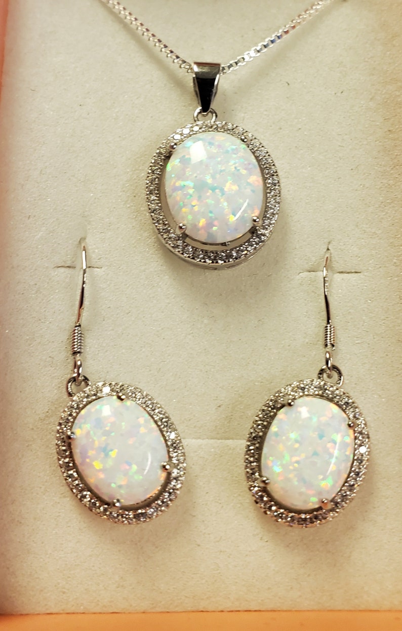 May include: A silver necklace and earrings set with oval-shaped white opal stones surrounded by a halo of smaller clear stones.