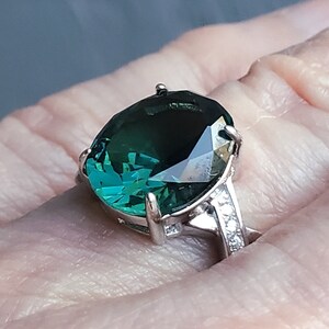 May include: A silver ring with a large, dark green gemstone. The gemstone is faceted and has a high polish.
