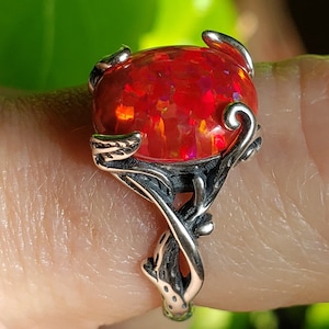 May include: A silver ring with a red opal gemstone set in a delicate, vine-like design.