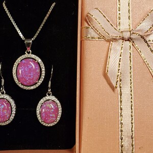 Puede incluir: Un conjunto de joyas de &oacute;palo rosa con un collar y pendientes. El collar tiene una cadena de plata y un colgante con una piedra de &oacute;palo rosa rodeada de un halo de plata. Los pendientes son de plata con piedras de &oacute;palo rosa rodeadas de un halo de plata.