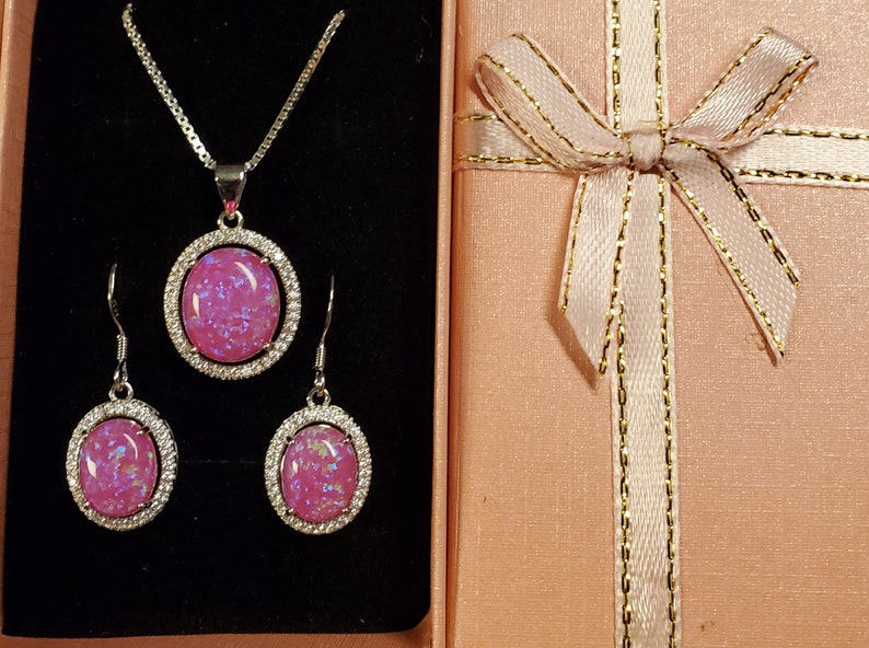 Puede incluir: Un conjunto de joyas de &oacute;palo rosa con un collar y pendientes. El collar tiene una cadena de plata y un colgante con una piedra de &oacute;palo rosa rodeada de un halo de plata. Los pendientes son de plata con piedras de &oacute;palo rosa rodeadas de un halo de plata.