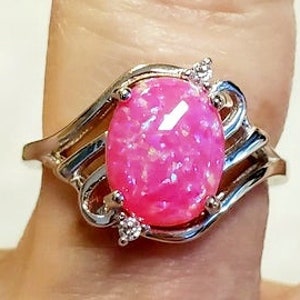 May include: A silver ring with a pink oval opal gemstone and two small clear gemstones on the band.