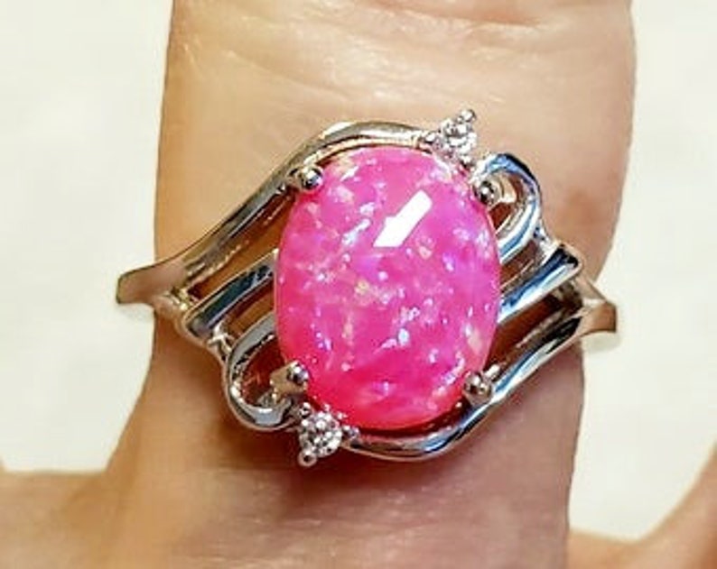 May include: A silver ring with a pink oval opal gemstone and two small clear gemstones on the band.