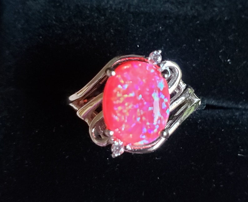 May include: A silver ring with a pink opal gemstone and two small clear stones on the band.
