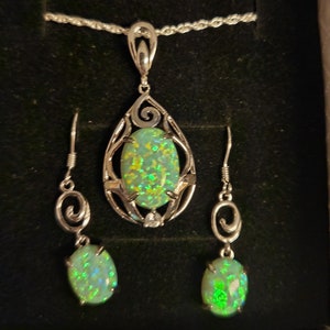 May include: A silver necklace and earrings set with a green opal pendant and matching earrings. The pendant is set in a silver filigree design.