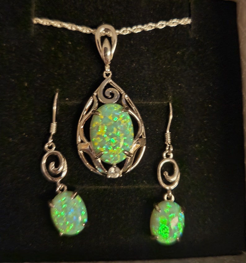 May include: A silver necklace and earrings set with a green opal pendant and matching earrings. The pendant is set in a silver filigree design.