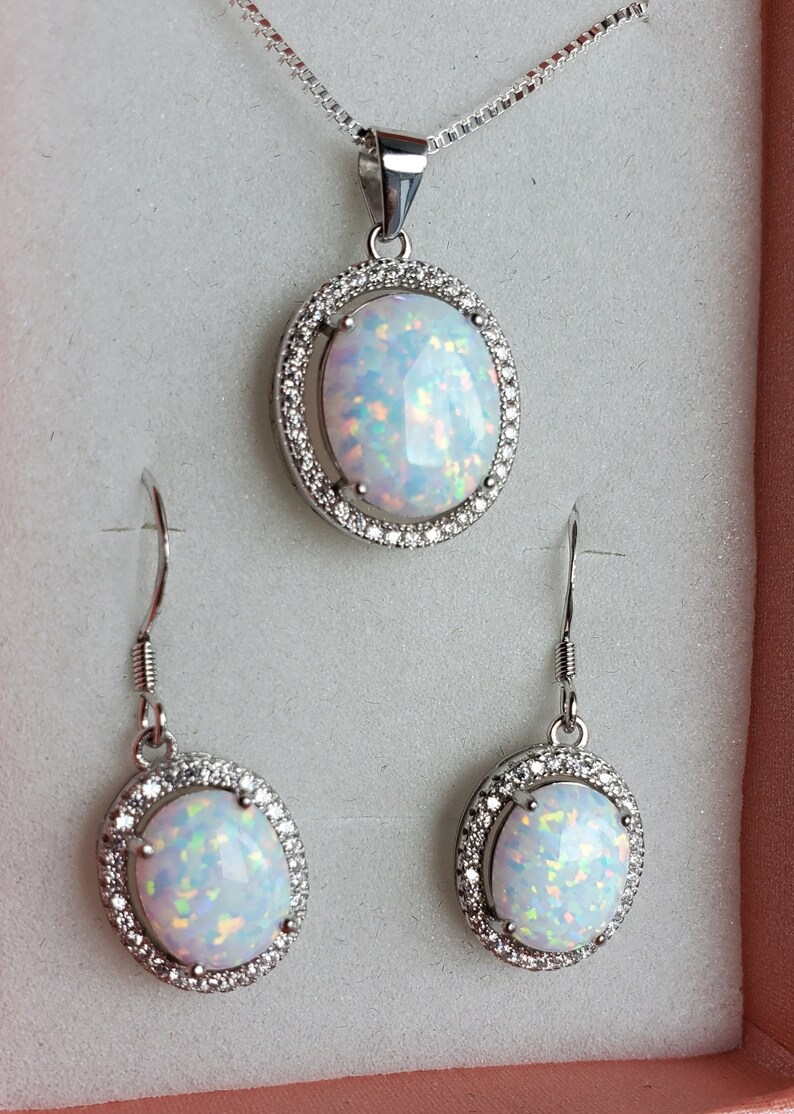 May include: A silver necklace and earrings set with a white opal stone in each piece. The stones are surrounded by a halo of smaller clear stones.