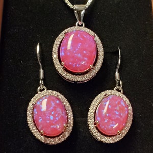 Puede incluir: Un conjunto de collar y pendientes de &oacute;palo rosa con una cadena de plata y un engaste de plata con piedras transparentes alrededor del &oacute;palo.