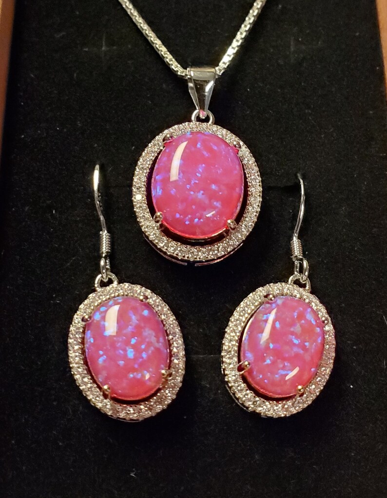 Puede incluir: Un conjunto de collar y pendientes de &oacute;palo rosa con una cadena de plata y un engaste de plata con piedras transparentes alrededor del &oacute;palo.