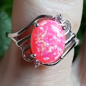 May include: A silver ring with a pink opal gemstone and two small clear stones. The ring has a wavy design.