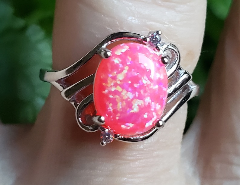 May include: A silver ring with a pink opal gemstone and two small clear stones. The ring has a wavy design.