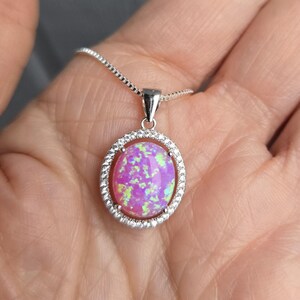 May include: A silver chain necklace with a pink opal pendant set in a silver oval frame with small clear stones around the edge.