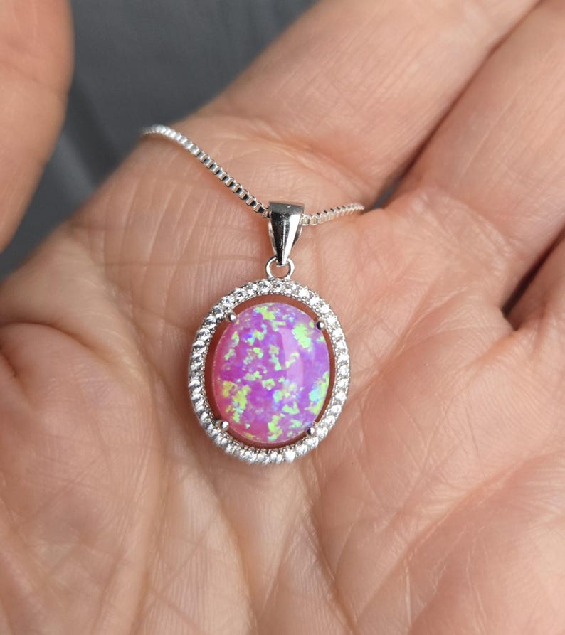 May include: A silver chain necklace with a pink opal pendant set in a silver oval frame with small clear stones around the edge.