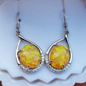May include: A pair of silver dangle earrings with yellow opal stones and clear cubic zirconia accents.