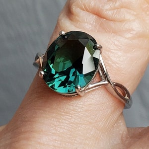 May include: A silver ring with a large, oval-shaped, dark green gemstone. The gemstone has a faceted cut and is set in a simple, elegant setting.