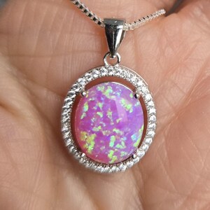 May include: A silver chain necklace with a pink opal pendant set in a silver oval frame with small clear stones around the edge.