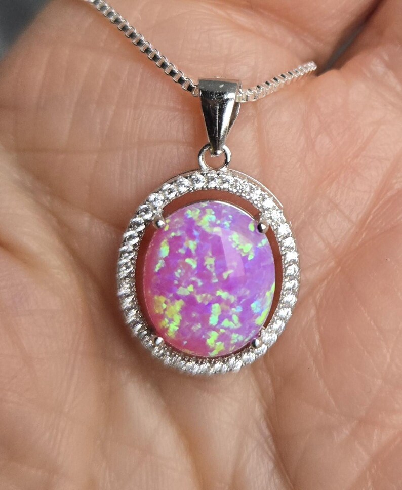 May include: A silver chain necklace with a pink opal pendant set in a silver oval frame with small clear stones around the edge.