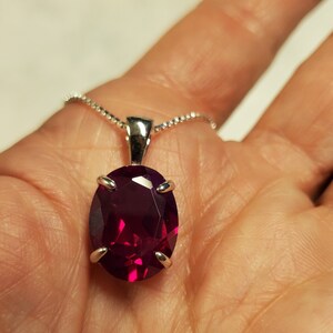 Puede incluir: Un collar de cadena de plata con un colgante de rub&iacute; de forma ovalada. El rub&iacute; es de color rojo intenso y tiene un corte facetado.