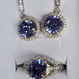 May include: A silver ring and a pair of earrings featuring a large, round, purple gemstone encircled by smaller, clear gemstones.
