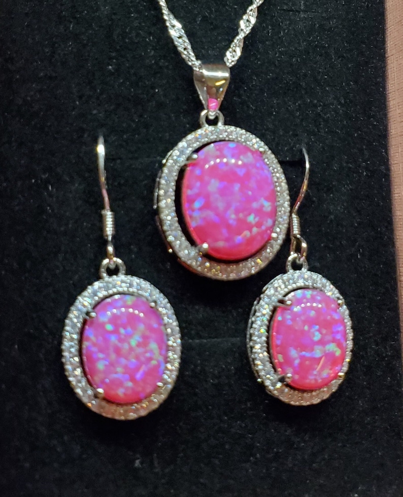 Puede incluir: Un conjunto de collar y pendientes de plata con piedras de &oacute;palo rosa rodeadas por un halo de circonita c&uacute;bica transparente.