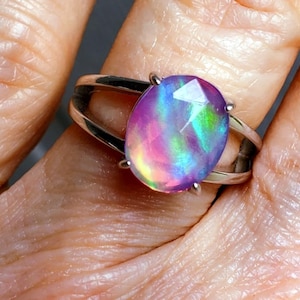 May include: A silver ring with a large oval-shaped opal gemstone. The opal is iridescent with shades of pink, purple, green, and blue.