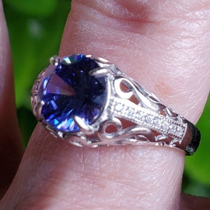 May include: A silver ring featuring a large, oval-shaped, dark blue gemstone set in a filigree design. The ring is accented with smaller, clear gemstones.