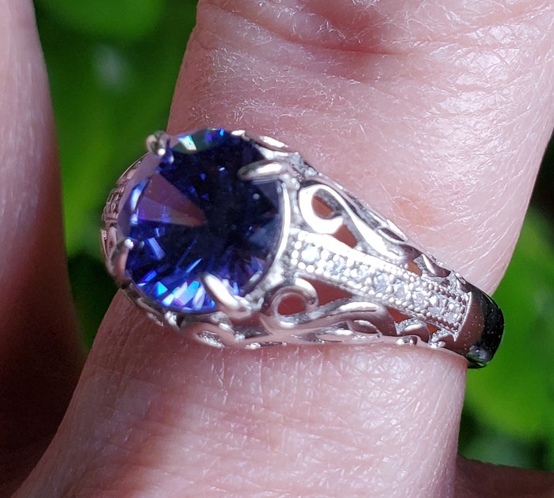 May include: A silver ring featuring a large, oval-shaped, dark blue gemstone set in a filigree design. The ring is accented with smaller, clear gemstones.