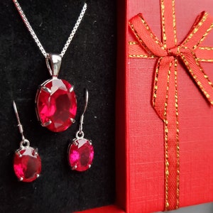 Puede incluir: Un conjunto de joyas de piedras preciosas rojas con un collar colgante y pendientes. El conjunto est&aacute; empaquetado en una caja de regalo roja con una cinta dorada.