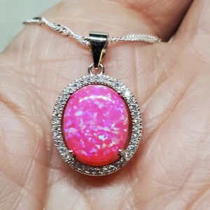Puede incluir: Un collar con un colgante de plata con una piedra de &oacute;palo rosa engastada en un marco ovalado de plata con piedras de circonita c&uacute;bica transparentes.