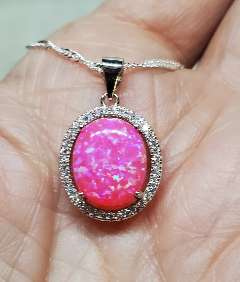 Puede incluir: Un collar con un colgante de plata con una piedra de &oacute;palo rosa engastada en un marco ovalado de plata con piedras de circonita c&uacute;bica transparentes.