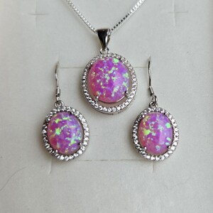 May include: A pink opal necklace and earrings set with a silver chain and oval-shaped stones surrounded by a halo of clear cubic zirconia.