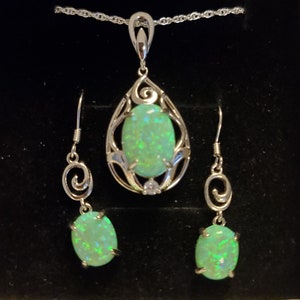 May include: A silver necklace and earrings set with a teardrop-shaped pendant and matching earrings. Each piece features a green opal stone surrounded by a delicate silver design.