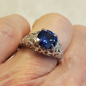 May include: A silver ring featuring a large, dark blue gemstone set in a filigree design.