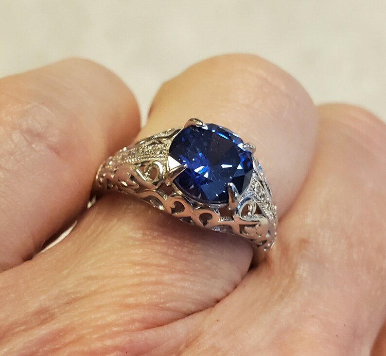 May include: A silver ring featuring a large, dark blue gemstone set in a filigree design.